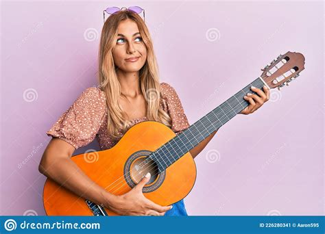 Beautiful Blonde Young Woman Playing Classical Guitar Smiling Looking