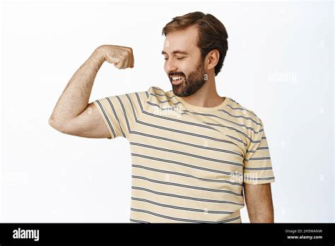 Portrait Of Smiling Pleased Man Looking At His Arm Muscles Flexing