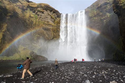 Tourists Taking Photos Of Waterfall Skogafoss Rainbow Around Them