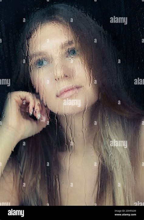 Portrait Of Young Blonde Woman Behind The Window Glass With Raindrops