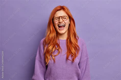 Emotional Ginger Woman Cannot Stop Laughing Keeps Mouth Widely Opened Poses Overjoyed Indoor