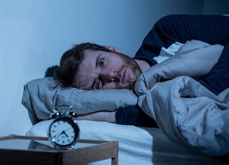 Young Man In Bed Staring At Alarm Clock Trying To Sleep Feeling Stressed And Sleepless Stock