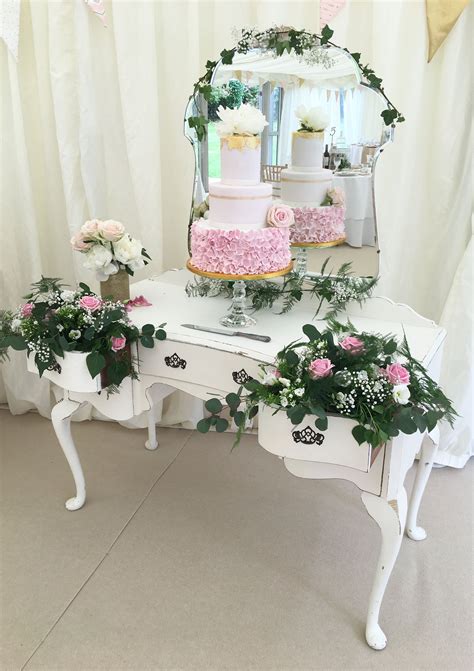 There Is A Table With Flowers On It And A Cake In The Mirror Behind It