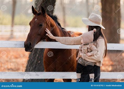 Young Mother And Little Baby Girl Near A Horses In Autumn Sunny Day