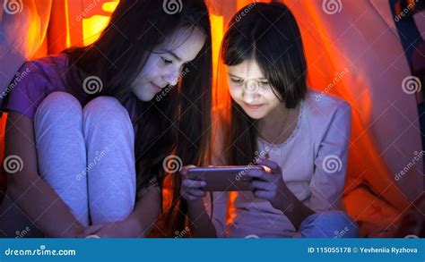 Portrait Of Two Teenage Girls In Pajamas Browsing Internet On Mobile