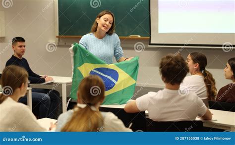 Confident Young Female Teacher Shows Students Flag Of Brazil Stock