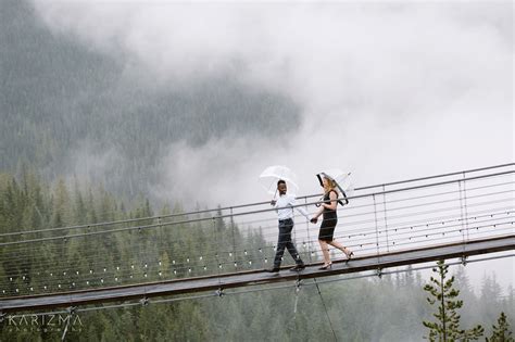 Couple Holding Hands Walking On The Suspension Bridge Holding Umbrellas Foggy Rainy Engagement