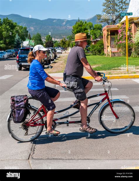 Middle Aged Couple Riding A Tandem Bicycle In The Small Mountain Town
