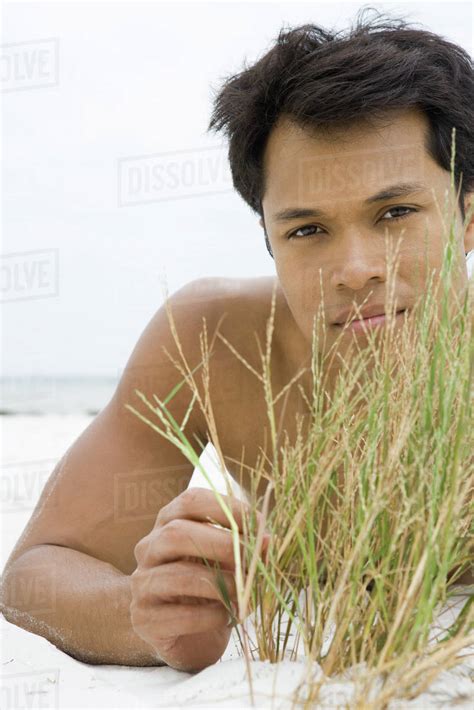 Man Lying On The Beach Touching Dune Grass Looking At Camera Stock