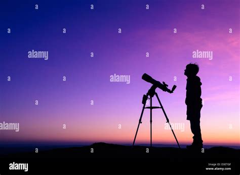 The Silhouette Of A Teenage Boy Stargazing With A Telescope At Dusk