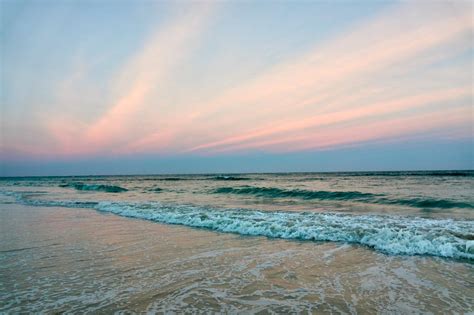 The Sky Is Pink And Blue Over The Water At Sunset On The Ocean Shore