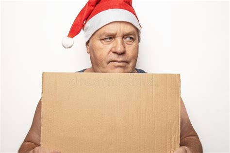 Funny Upset And Angry Mature Man In Red Christmas Santa Hat Holds Cardboard Sign With
