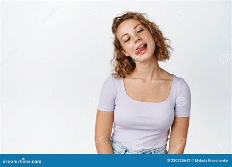 Funny Blond Girl Showing Tongue Fooling Around And Squinting Standing Against White Background