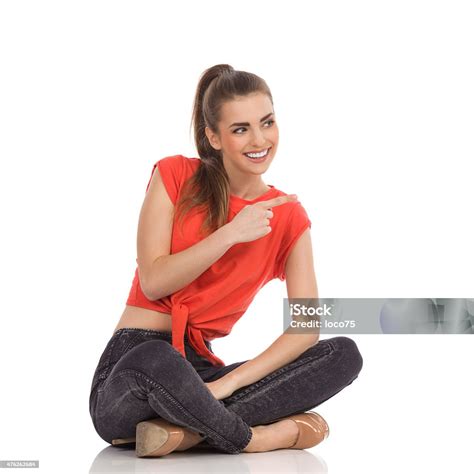 Young Woman Sitting With Legs Crossed And Pointing Stock Photo
