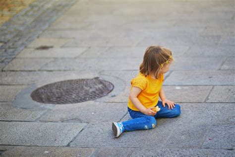 Unhappy And Stubborn Toddler Girl Sitting On The Floor Outdoors Stock