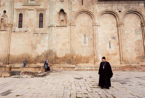 Christian Priest Standing Near The Ornamental Stone Wall Of