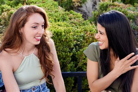 Dos Amigas Hablando Y Riendo Mientras Se Sientan En Un Banco En Un