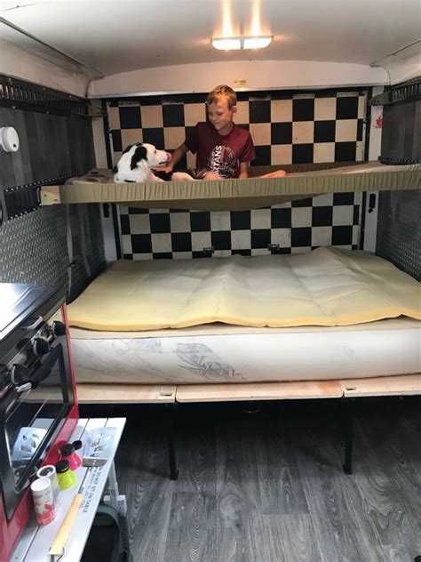 A Man Sitting In The Back Of A Truck With Two Bunk Beds On Top Of It