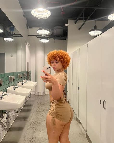 A Woman Taking A Selfie In A Public Restroom With Sinks And Urinals