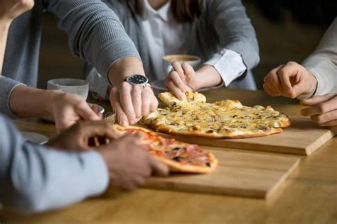Hands Of Diverse People Taking Pizza Slices Dining In Pizzeria Stock