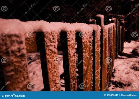Snow Covered Rural Wooden Fence In The Night Illuminated By Warm Street