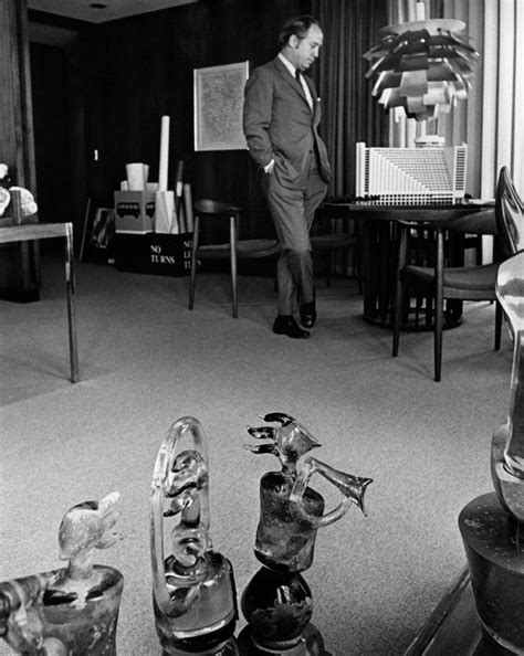 A Man Standing In A Living Room Next To Glass Vases And Other Items On