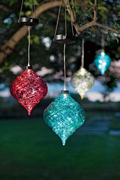 Three Glass Ornaments Hanging From A Tree In Front Of A Green Lawn And