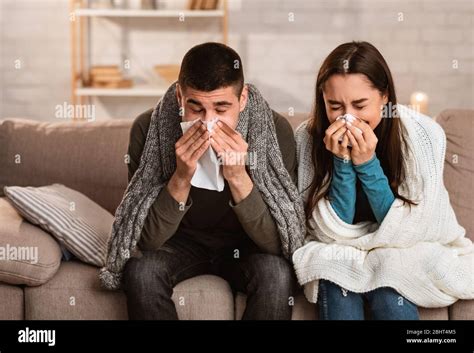 Sick Young Couple Blowing Noses Sitting On Couch Having Flu Stock