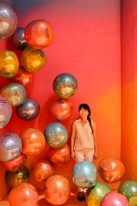 a woman is standing in front of many balloons that are floating up and down the wall