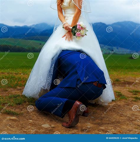Groom Peeking Under His Bride Dress Funny Wedding Concept Stock