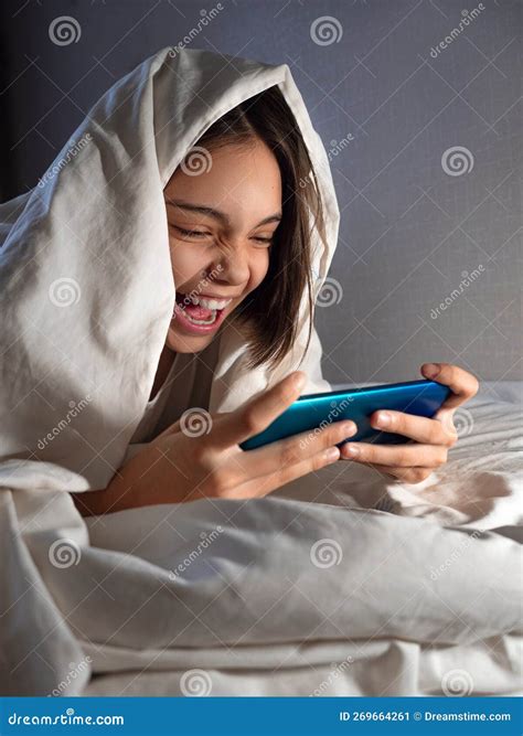 teenager girl playing with her smartphone at night in bed under the blanket vertical photo