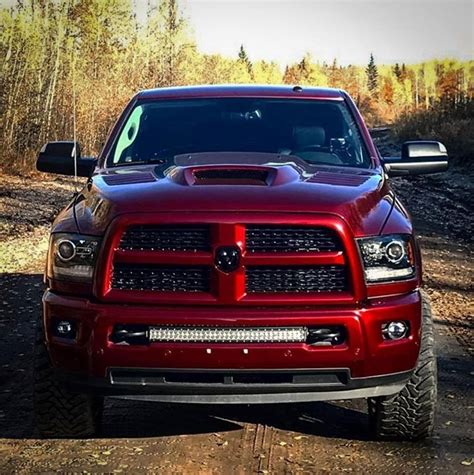 The Front End Of A Red Ram Truck Parked On A Dirt Road Near Some Trees