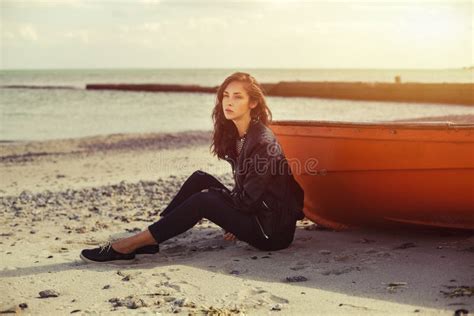 A Girl Sideways Near A Red Boat On The Beach By The Sea Stock Photo