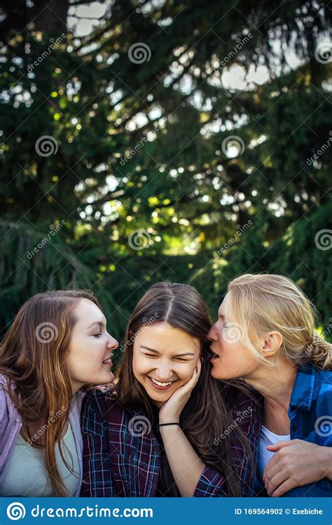 Three Cheerful Girls Whisper And Gossip Against Green Foliage In The Park Women Joke And Laugh