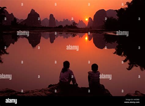 A Little Girl And Boy Gazing At Li River And Karst Hills At Sunset On