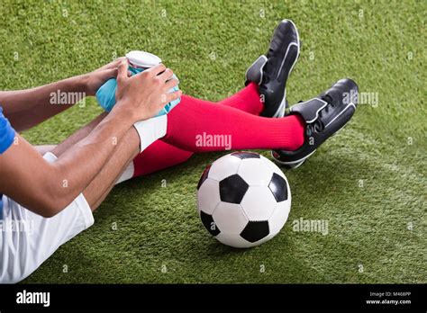 Close Up Of An Injured Male Soccer Player Applying Ice Pack On Knee