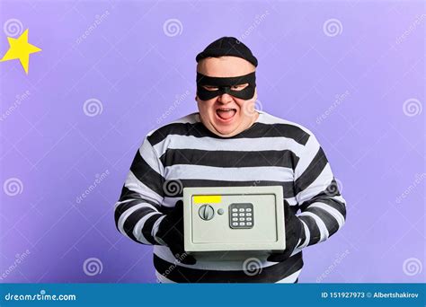 happy cheerful excited burglar in mask and striped clothes holding safety box stock image