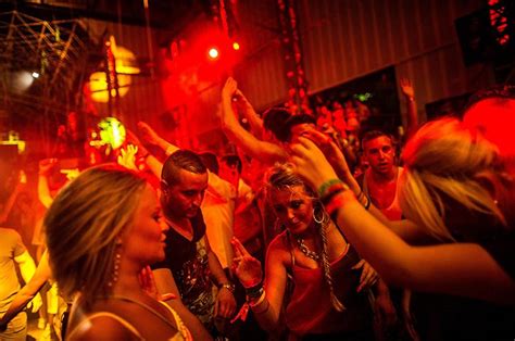 A Group Of People Standing Around Each Other In A Room With Red Lights On The Ceiling