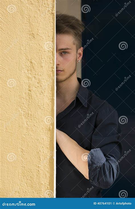 Attractive Young Blond Man Hiding Half Face Behind Wall Stock Photo