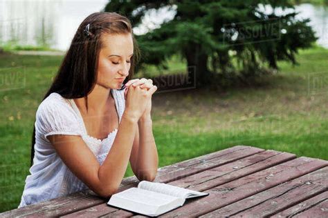 Young Woman Reading Her Bible And Praying Outdoors In A Park St