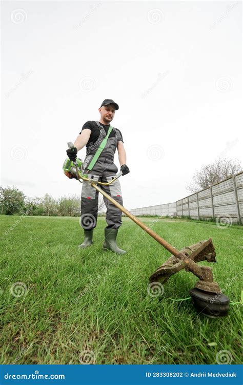 Professional Gardener In A Uniform Is Trimming The Green Grass Male