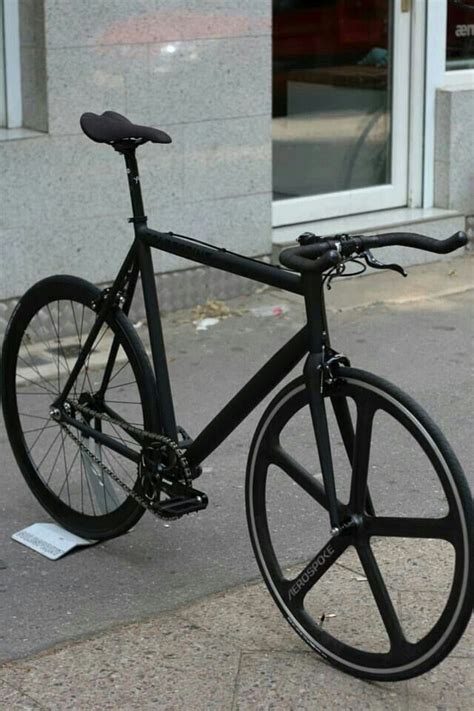 A Black Bike Parked On The Side Of A Street Next To A Building With Windows