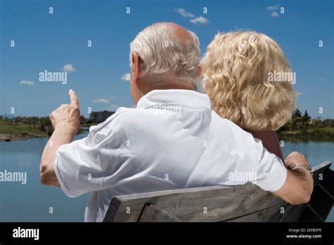 Rear View Of A Senior Couple Sitting On A Bench At The Lakeside Stock