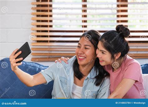 Happy Asian Lesbian Couple Using Mobile Video Call With Friend At Sofa In Living Room At Cozy