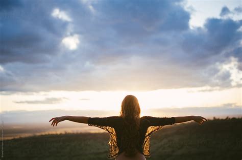 Woman With Red Hair Facing Sunset With Arms Outstretched By Stocksy