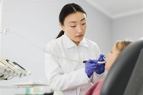 Female Asian Dentist In White Uniform Making Dental Check Up And Caries Treatment With Drill