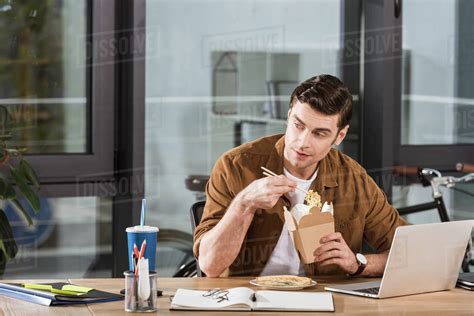 Handsome Businessman Eating Take Away Noodles From Box At Office