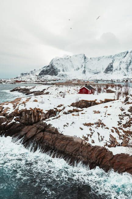 Red Cabins Located On Mountain Range Snowy Coast On Lofoten Islands