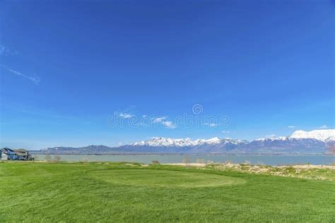 Lush Grassy Terrain With View Of A Calm Lake And Towering Snow Topped
