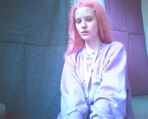 A Woman With Pink Hair Sitting In Front Of A Window